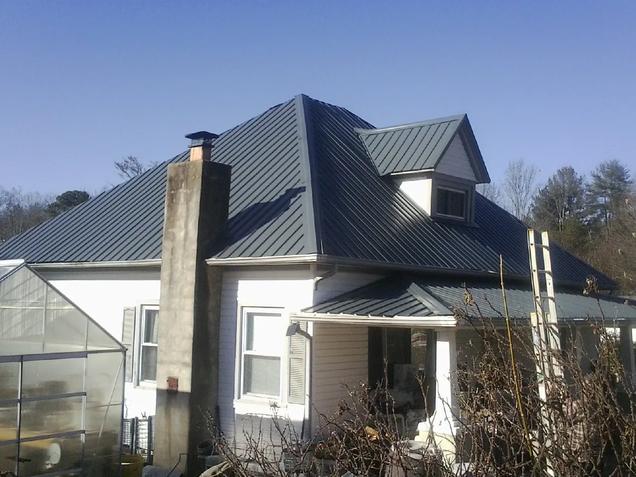 Dark blue standing seam metal roof on a white farmhouse with dormer — Slate & Tile Roof Repair by Roofing Brothers in Maple Plain