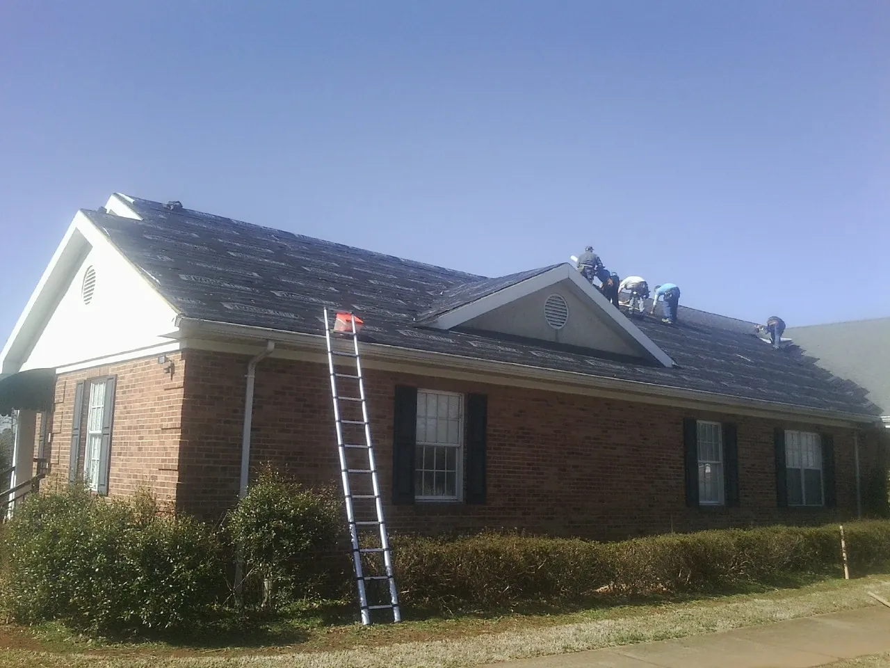Crew tearing shingles off a brick ranch roof with a ladder set — Emergency Roof Repair work by our crew in Maple Plain