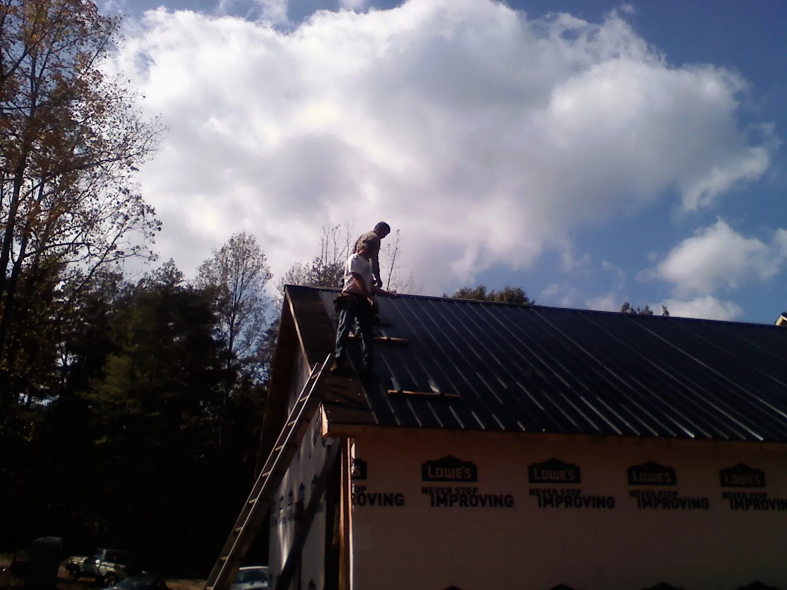 Roofer fastening dark metal panels high against a cloudy sky, from a Roof Inspection job in Maple Plain